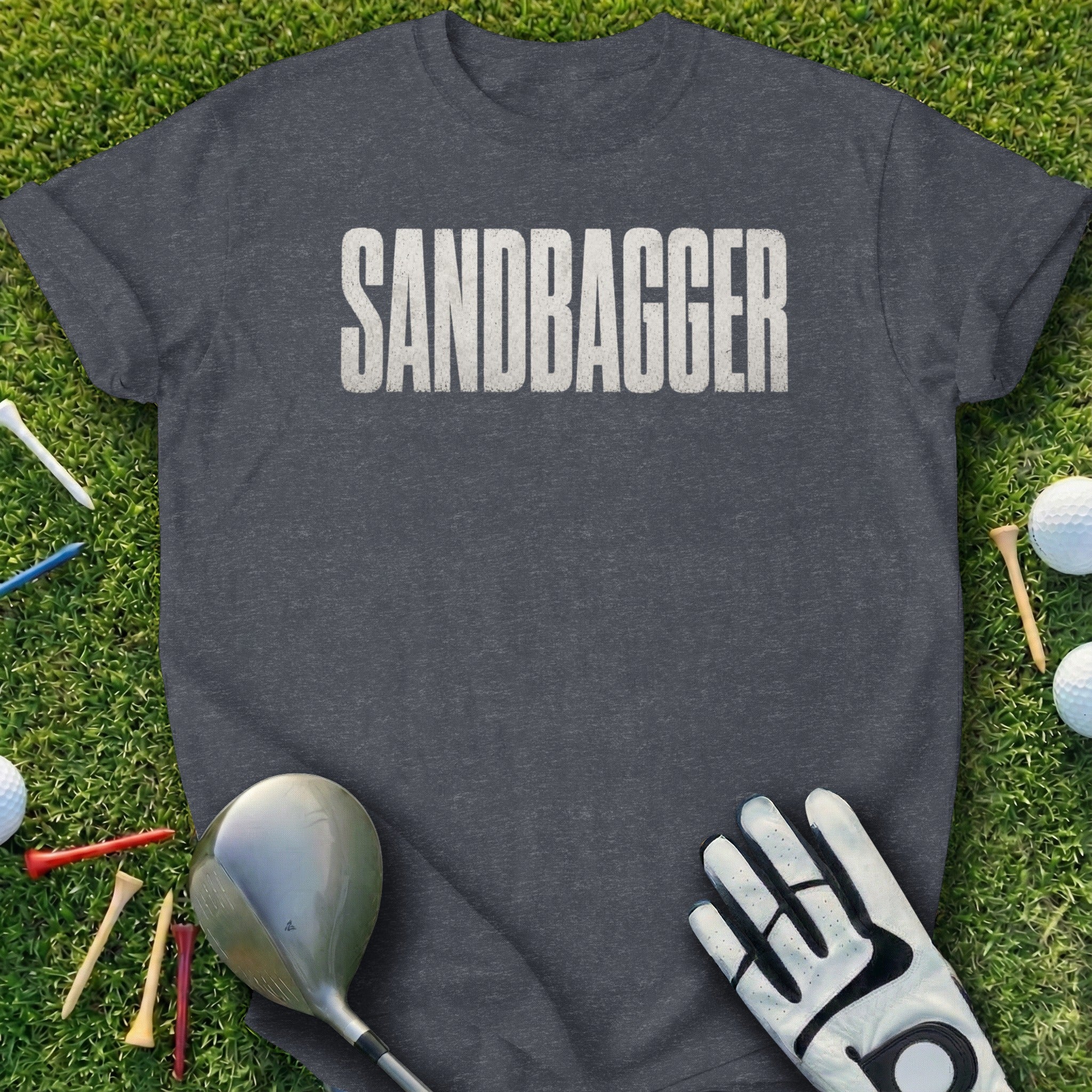Dark grey t-shirt with "SANDBAGGER" in white distressed lettering on grass.