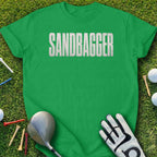 Green t-shirt with "SANDBAGGER" in large white letters on grass with golf items.
