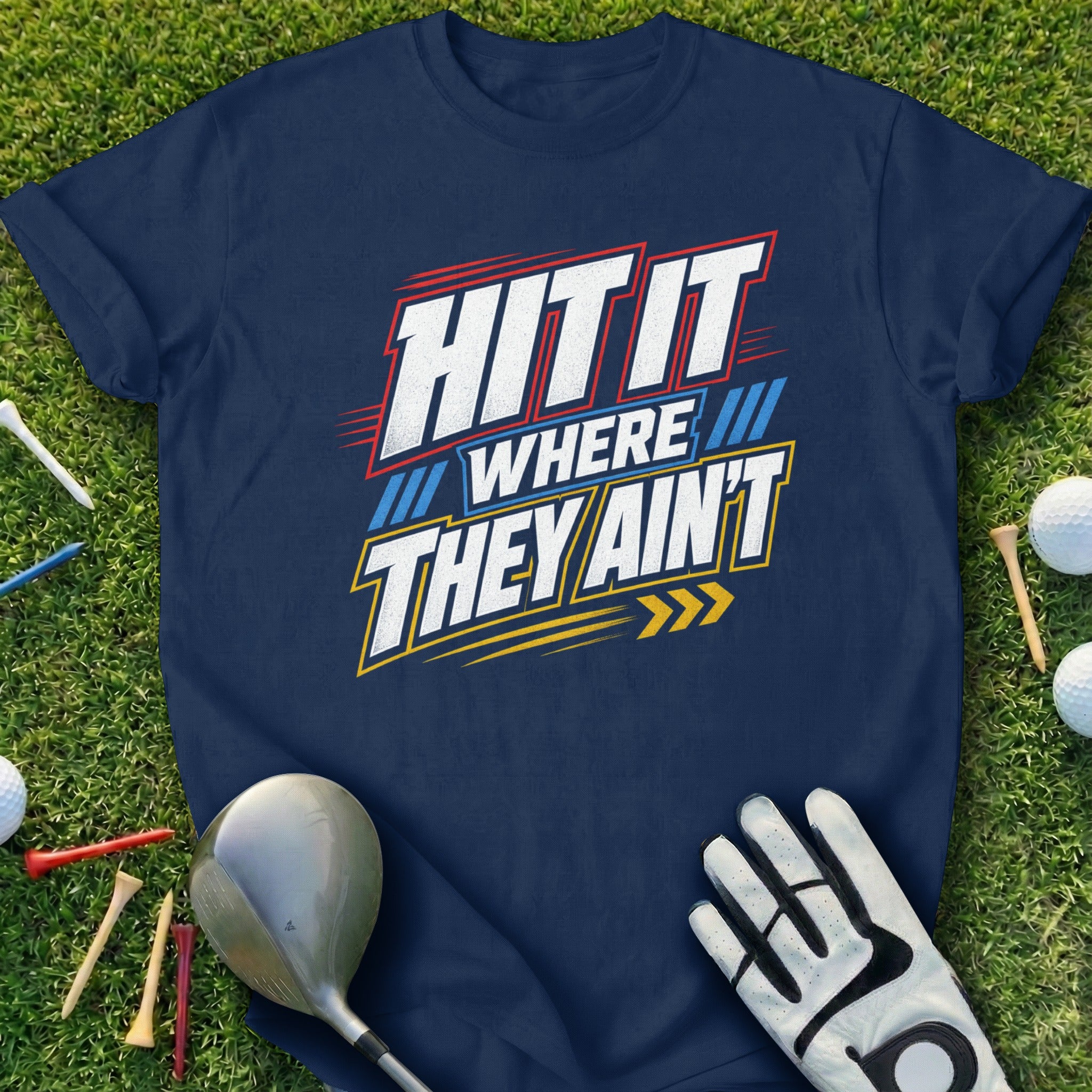 Navy t-shirt with "HIT IT WHERE THEY AIN'T" slogan and golf accessories on grass.