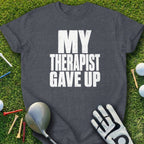 Dark grey t-shirt with "MY THERAPIST GAVE UP" text, golf club, glove, and tees.
