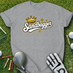 Grey t-shirt with "Sandbagger" logo, golf glove, club, and balls on grass.