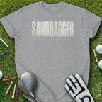 Gray t-shirt with "SANDBagger" text and golf accessories on grass.
