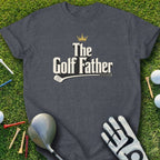Dark gray t-shirt with "The Golf Father" and crown graphic, on grass with golf items.